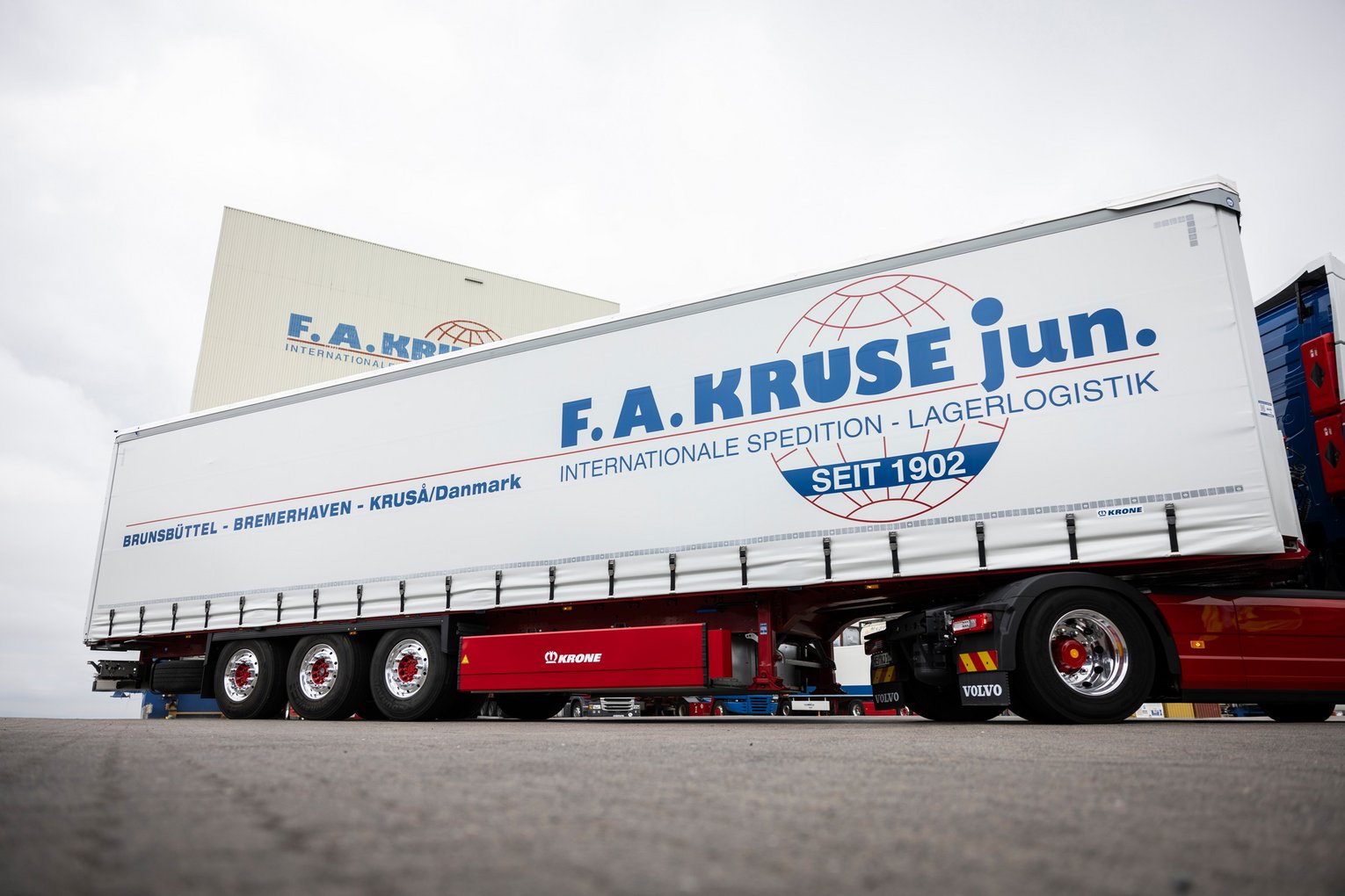 Sattelzug mit F.A. Kruse jun.-Logo vor Halle Sattelzug mit weißem Auflieger und F.A. Kruse jun.-Logo steht vor einer Lagerhalle.