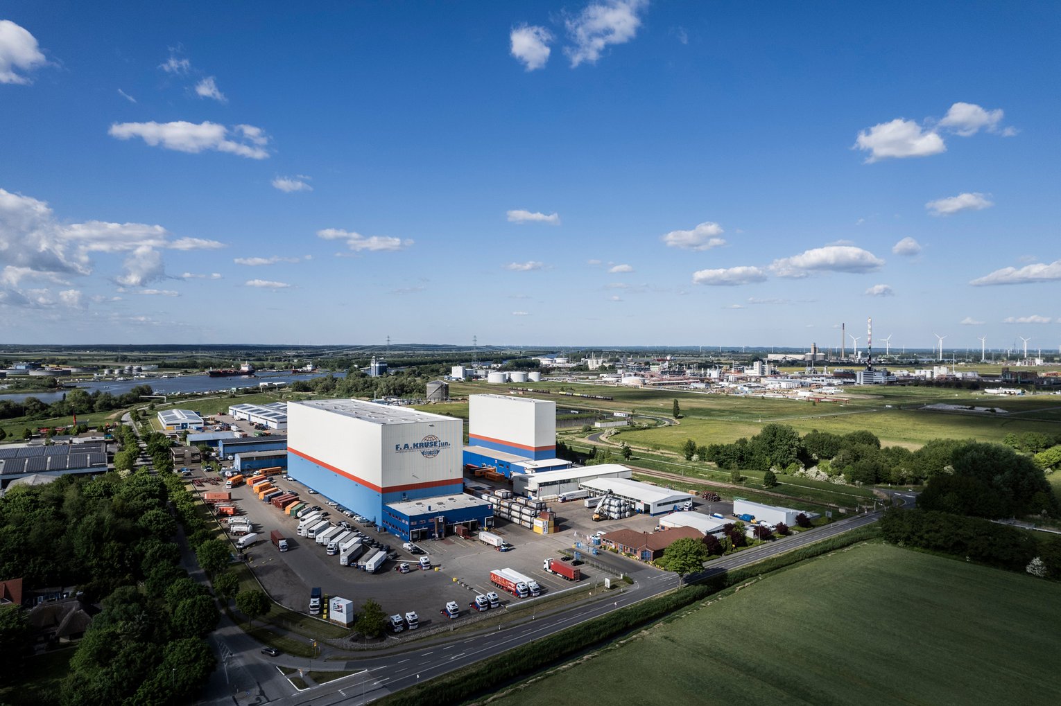 Logistikzentrum mit Hochregallagern und Flussblick Luftaufnahme eines modernen Logistikzentrums mit zwei Hochregallagern, Parkplatz und Fluss im Hintergrund.